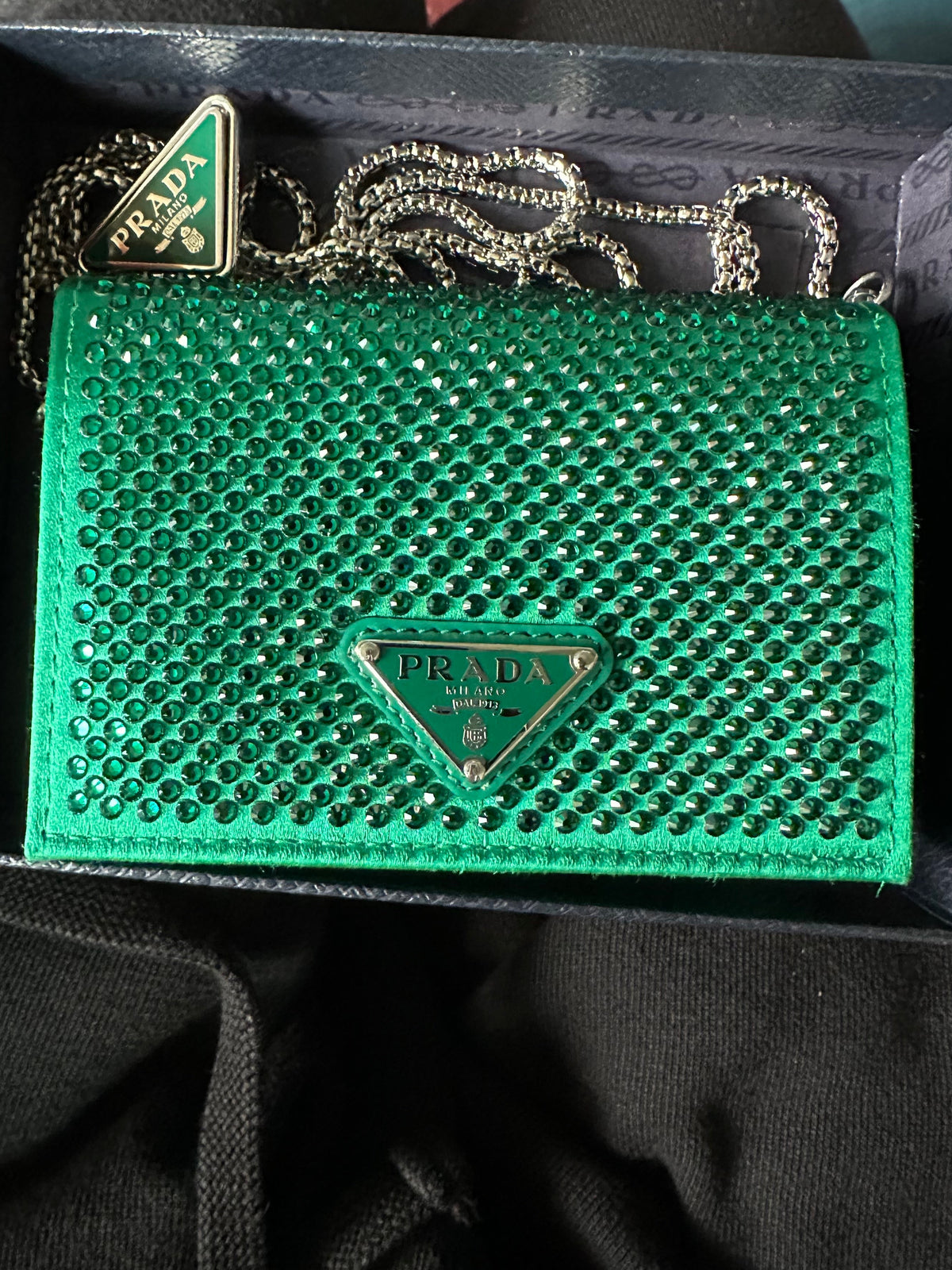 A green Prada card holder with a rhinestone-embellished surface and a silver-tone chain, presented in its original dark box. 